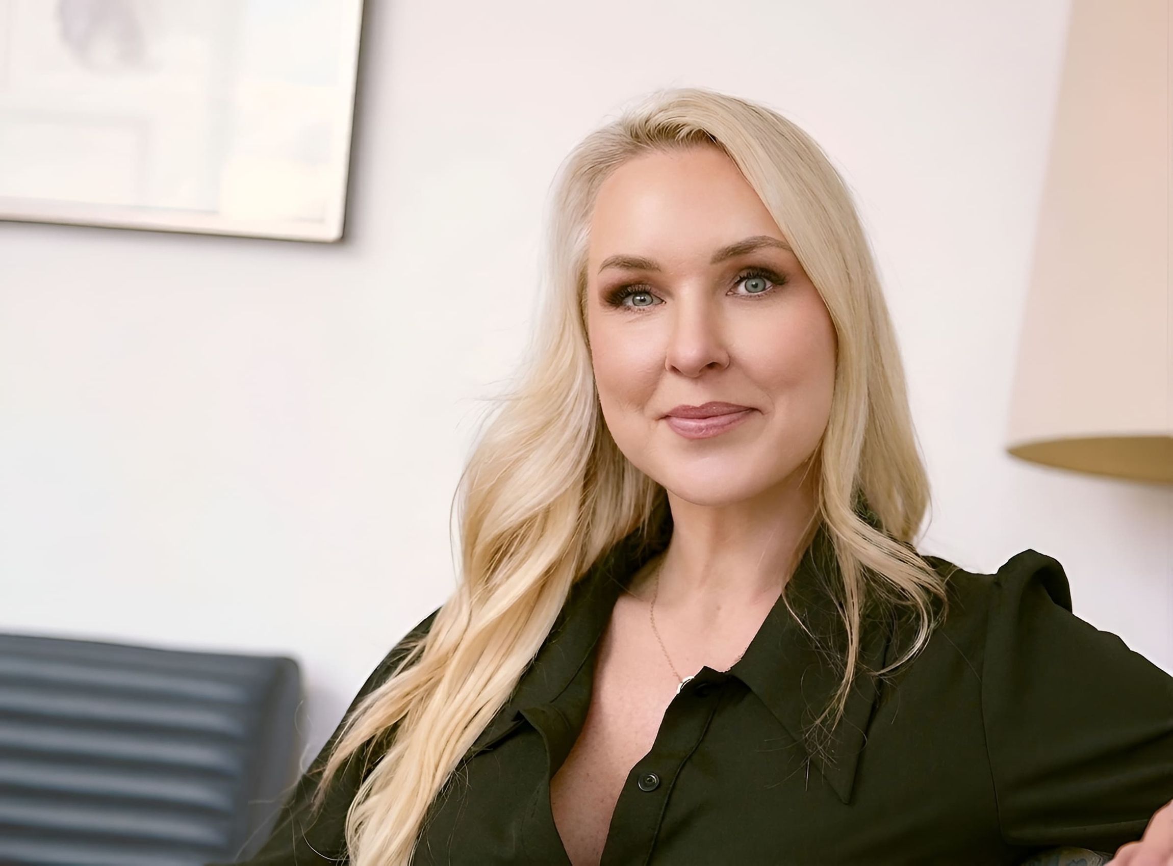Dr. Karen Stewart in a black blouse is sitting relaxed on a sofa in a modern, bright office.