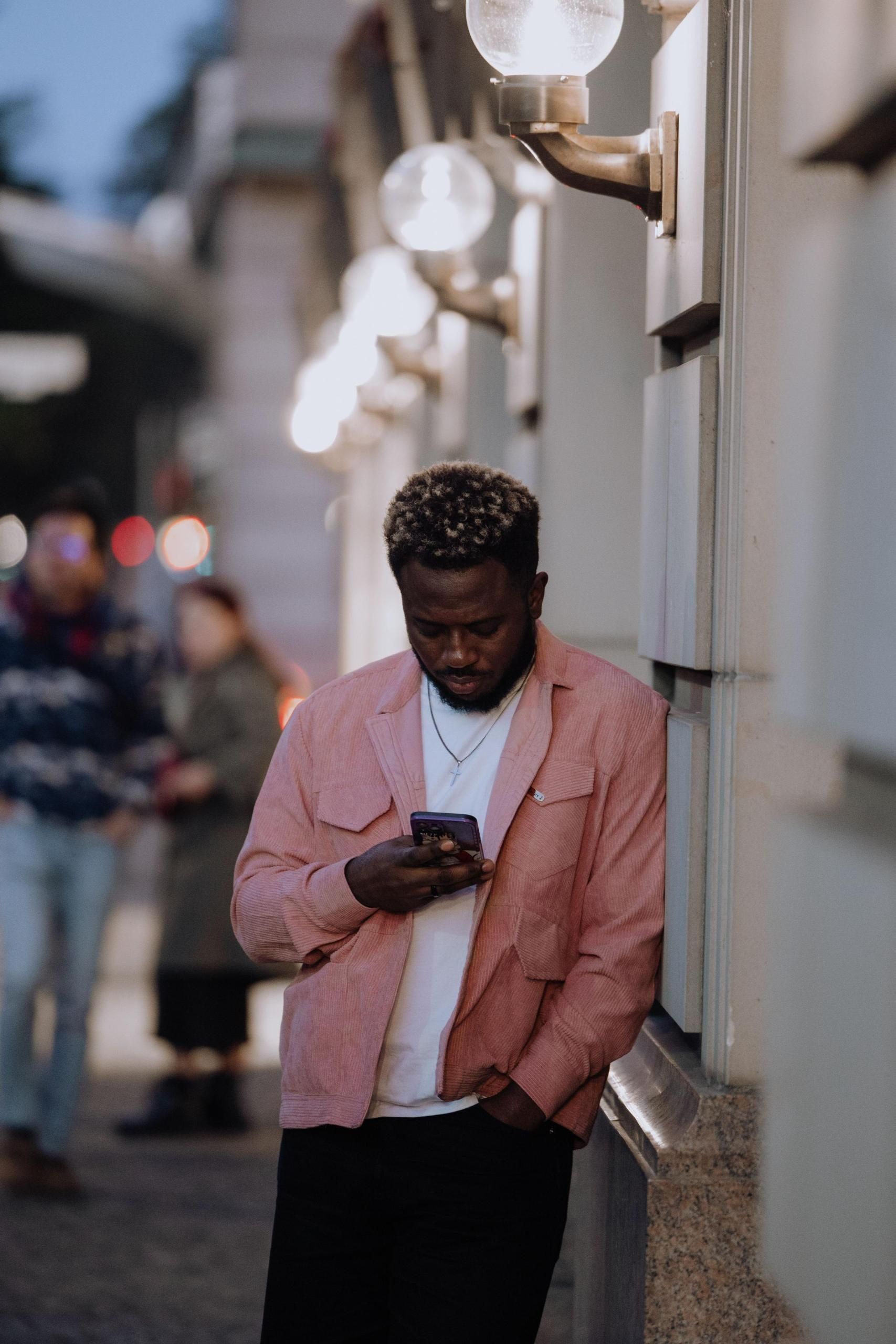 Man in pink shirt standing on the street looking down on his phone.
