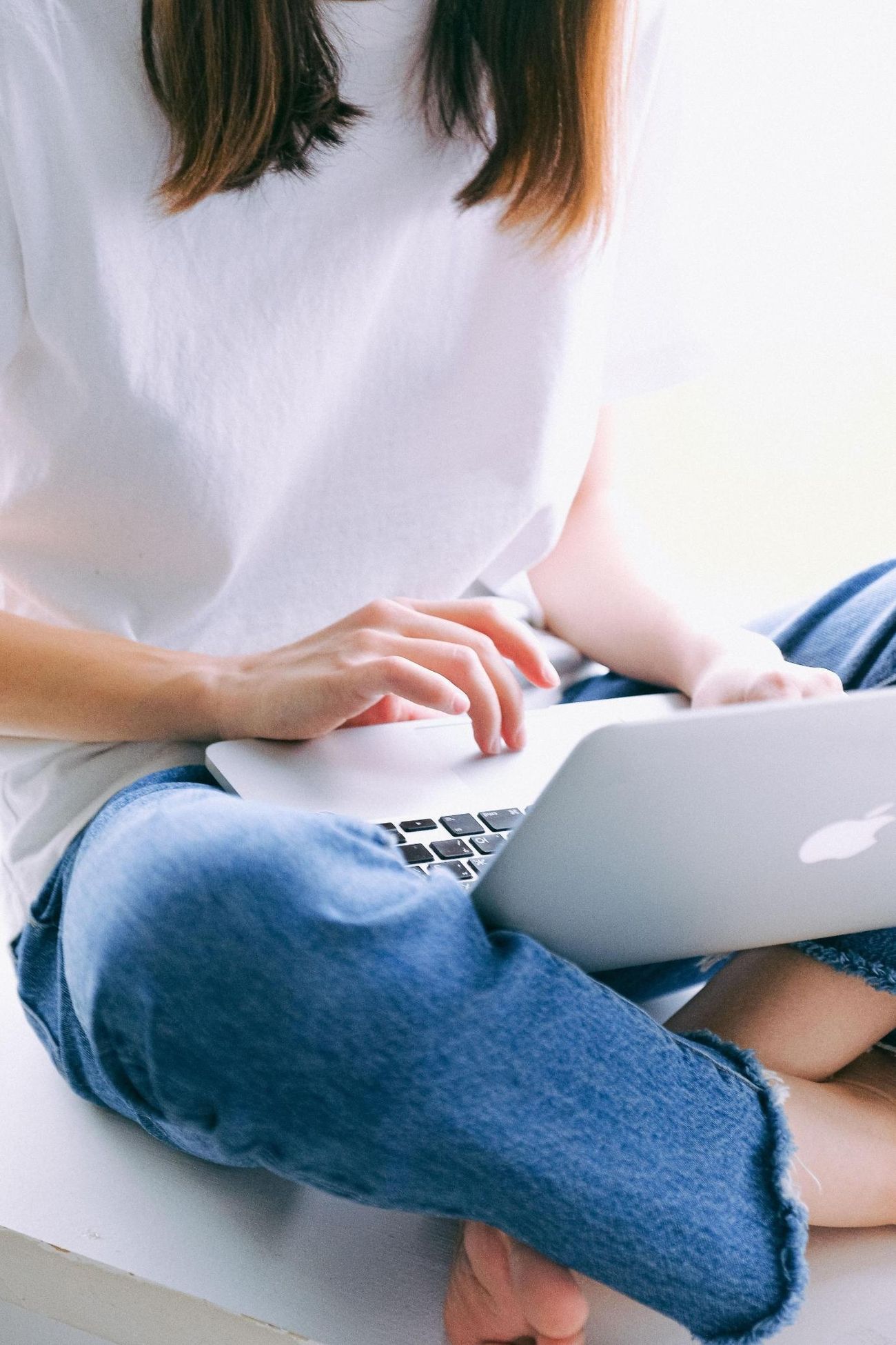 Woman in white shirt and jeans sitting and using her laptop
